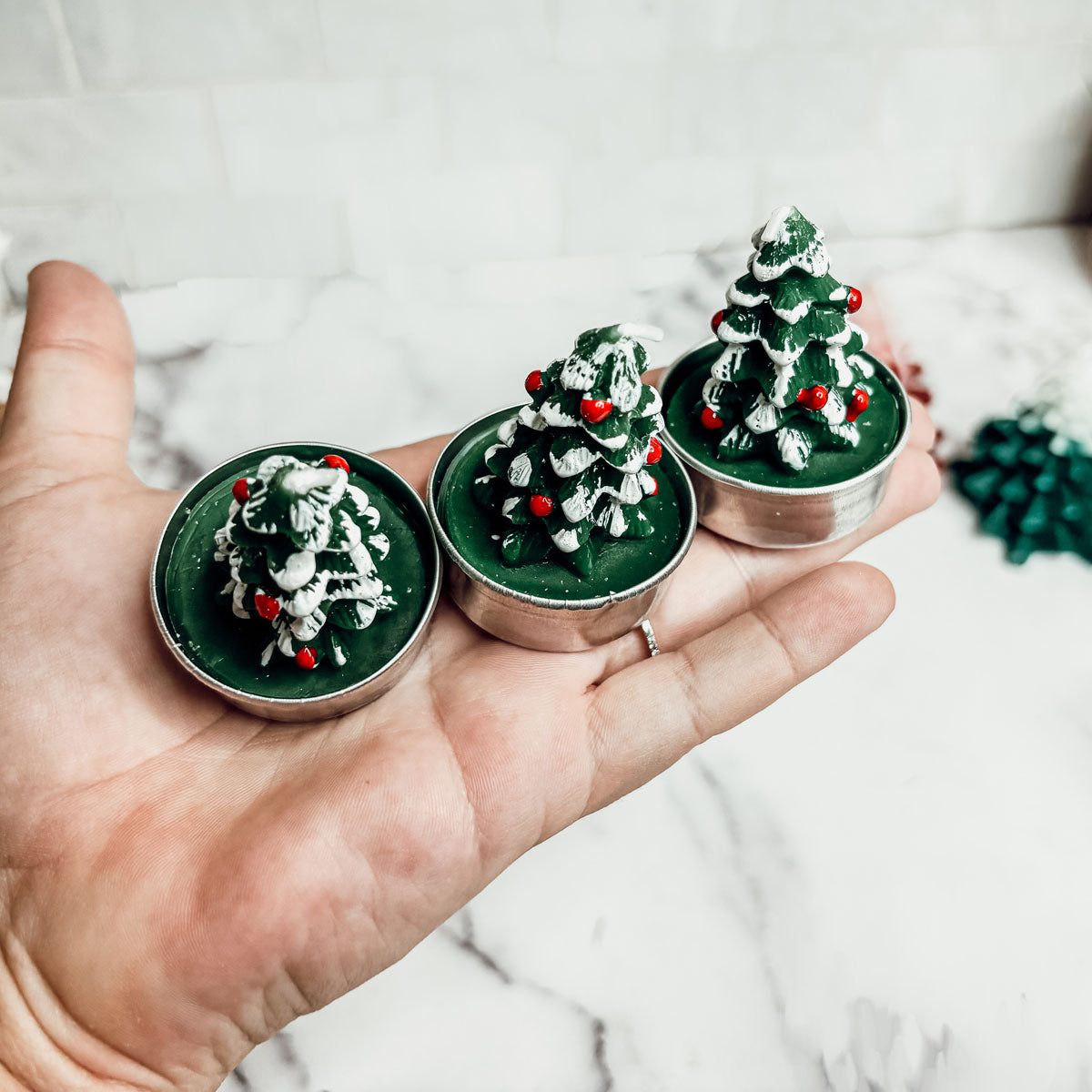 Three small Christmas tree-shaped candles held in a hand against a white background