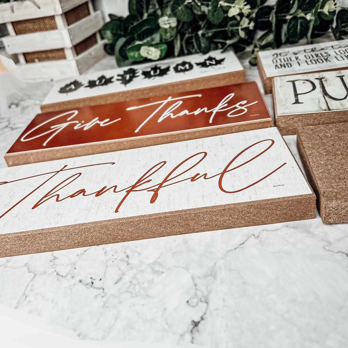 Decorative wooden signs with 'Give Thanks' and 'Thankful' text on a marble surface.