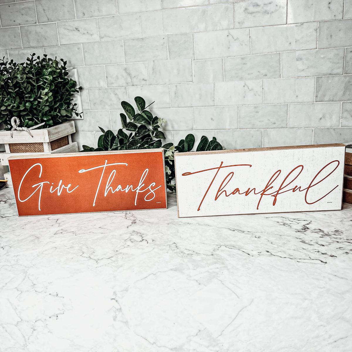 Two wooden signs with 'Give Thanks' and 'Thankful' text on a marble surface.