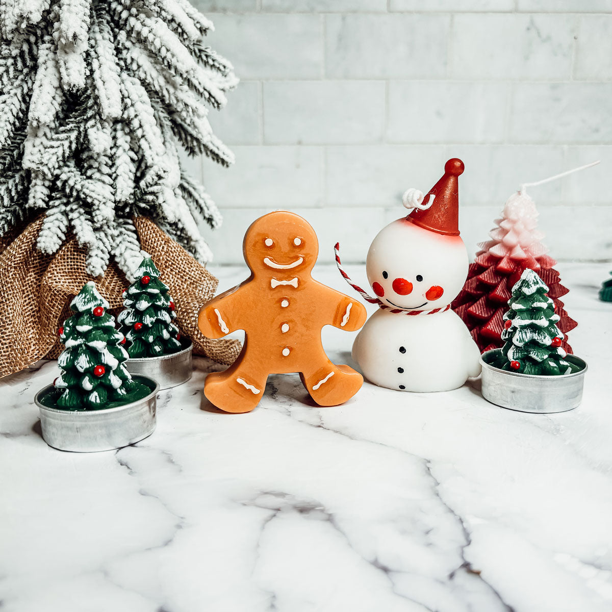 Decorative Christmas scene with gingerbread man, snowman, and small trees on a marble surface.