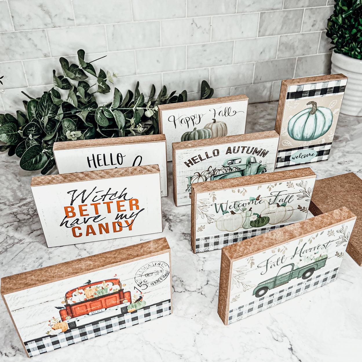 Set of decorative fall-themed signs on a marble surface with plants in the background.