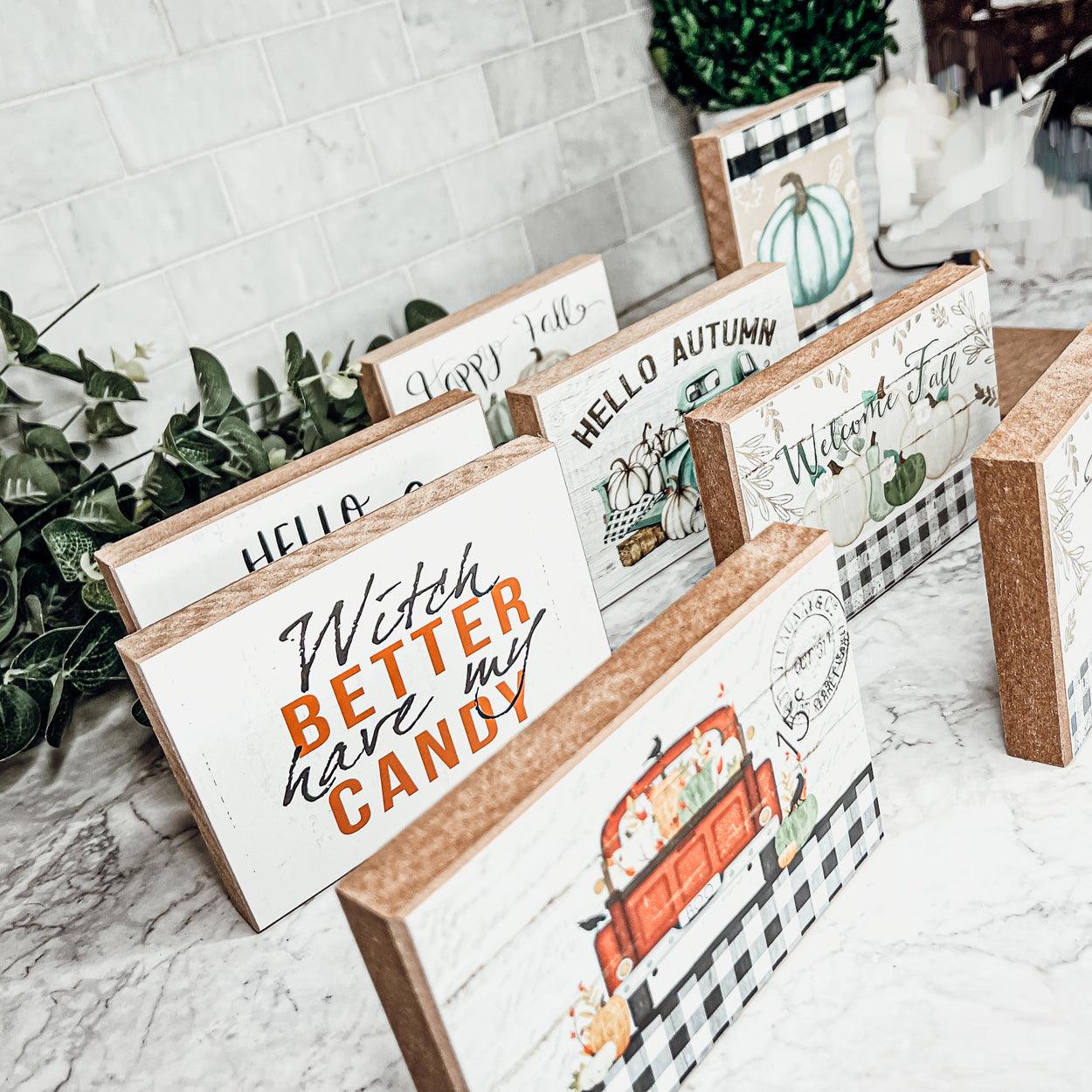 Decorative sign blocks with autumn-themed designs on a marble surface.