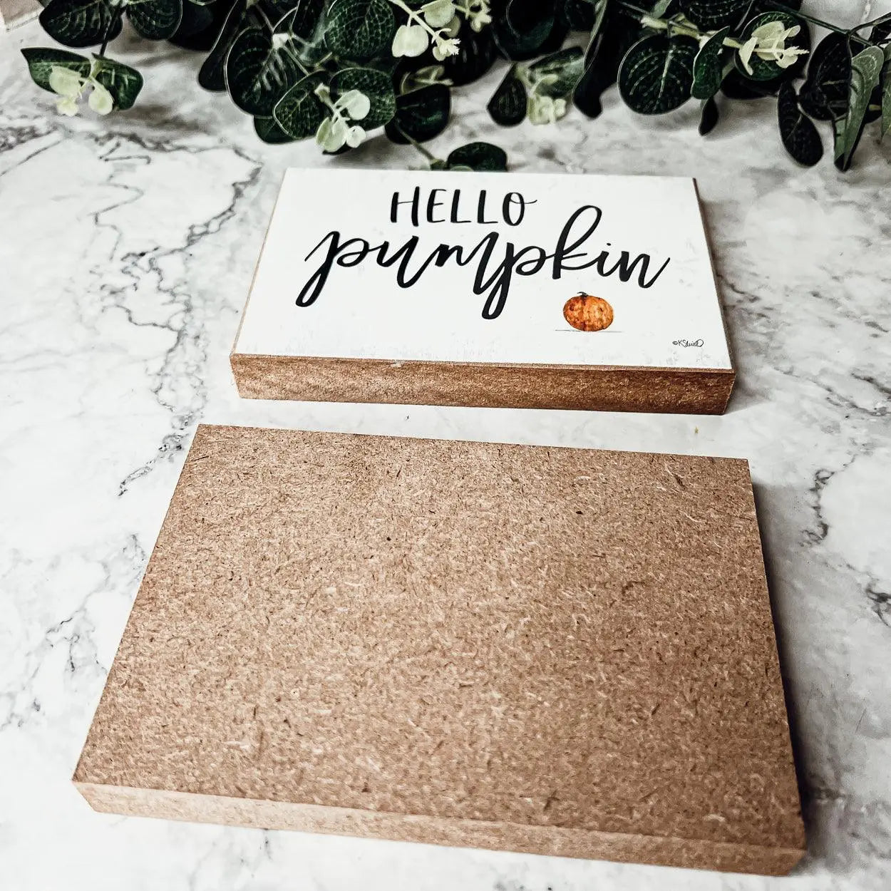 Cork board with 'Hello Pumpkin' text on a marble surface with greenery.