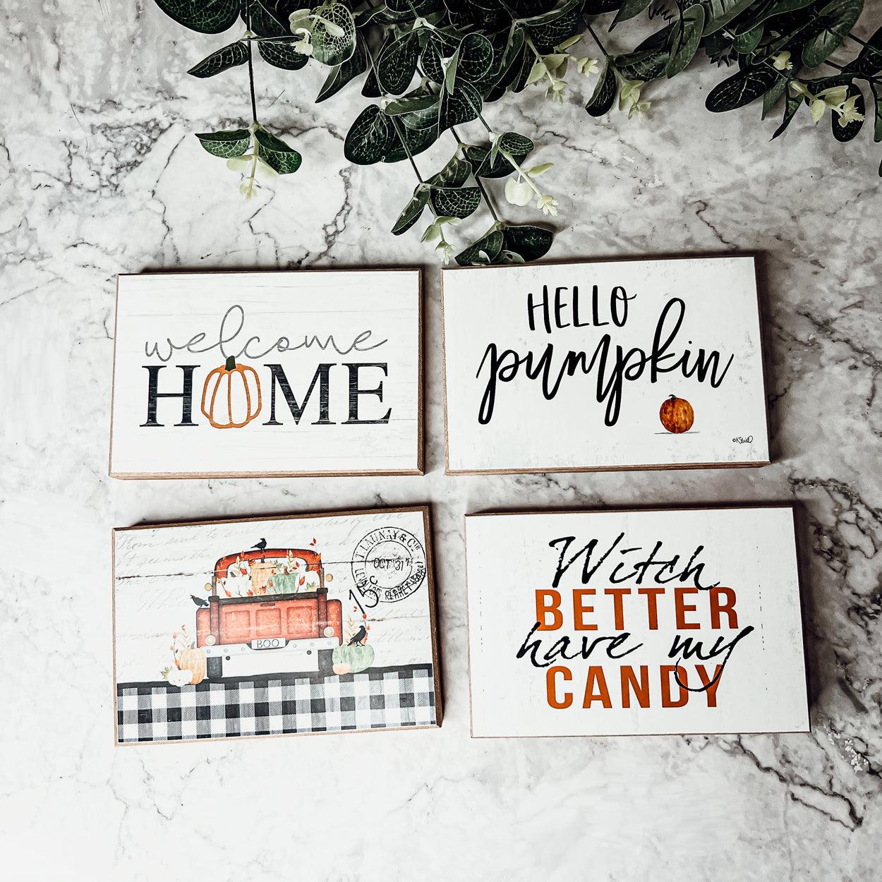 Four autumn-themed signs on a marble surface with greenery.