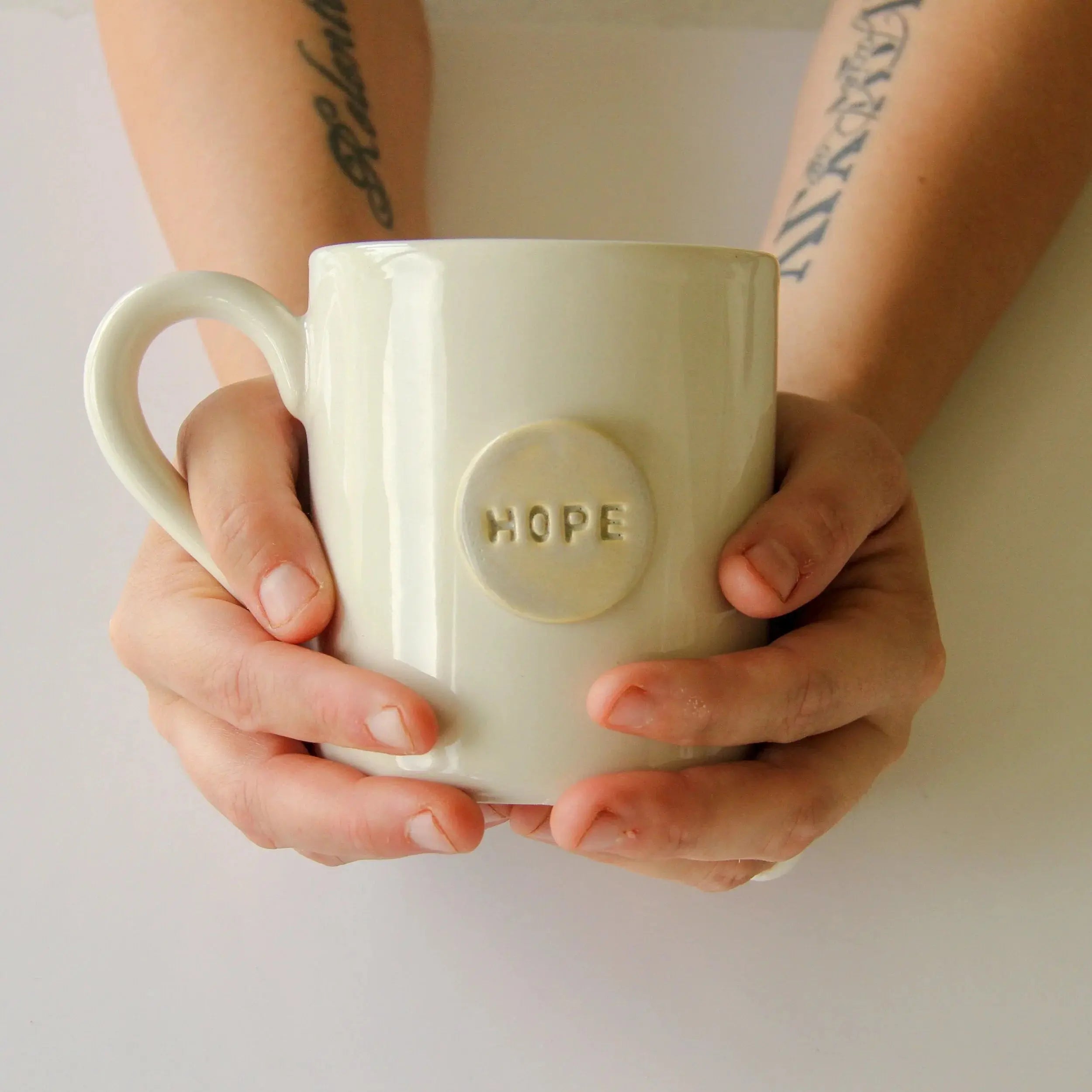 Cream ceramic mug with 'HOPE' embossed, held in hands — cozy farmhouse decor