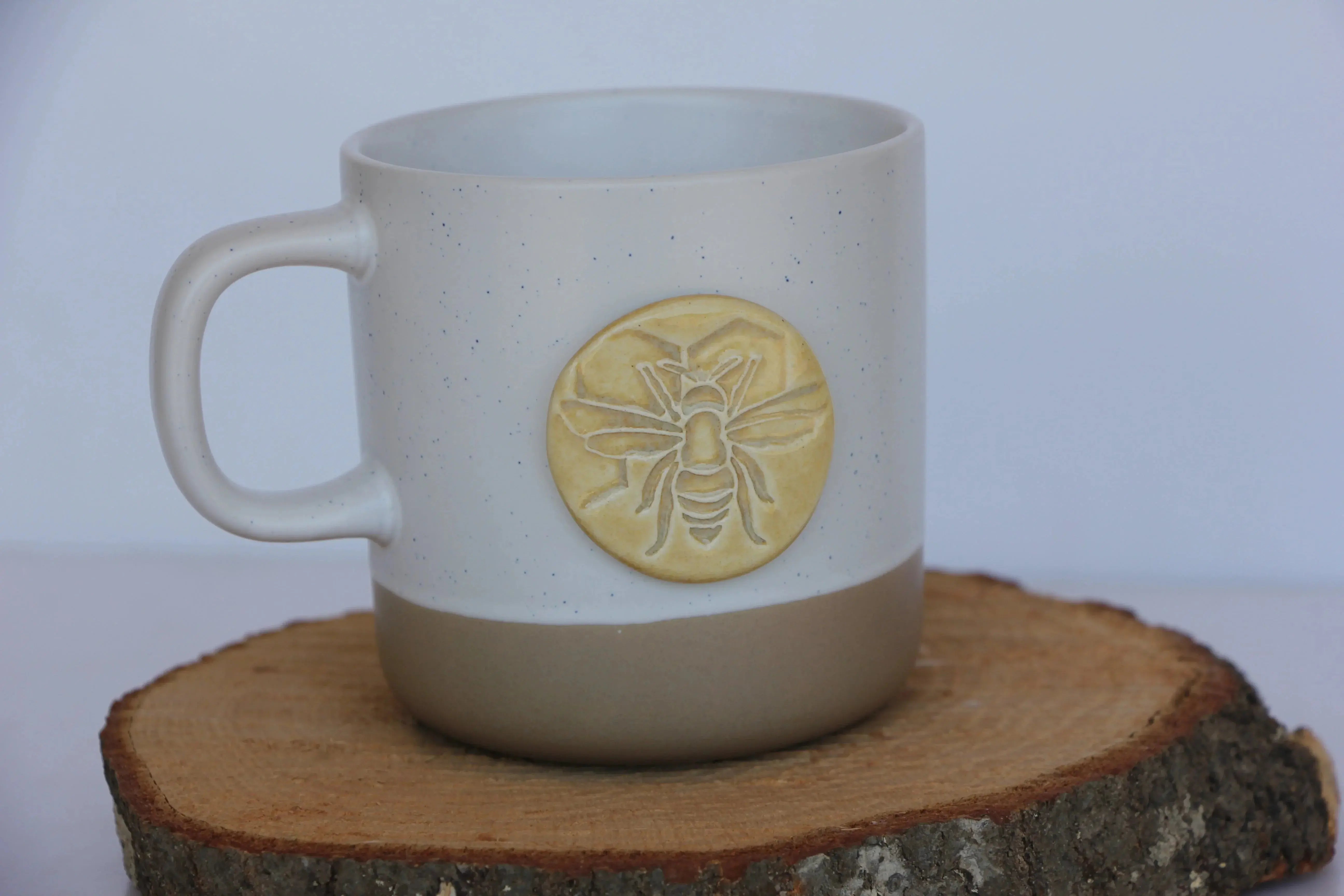 Speckled ceramic mug with bee design, farmhouse style coffee cup on wood slice