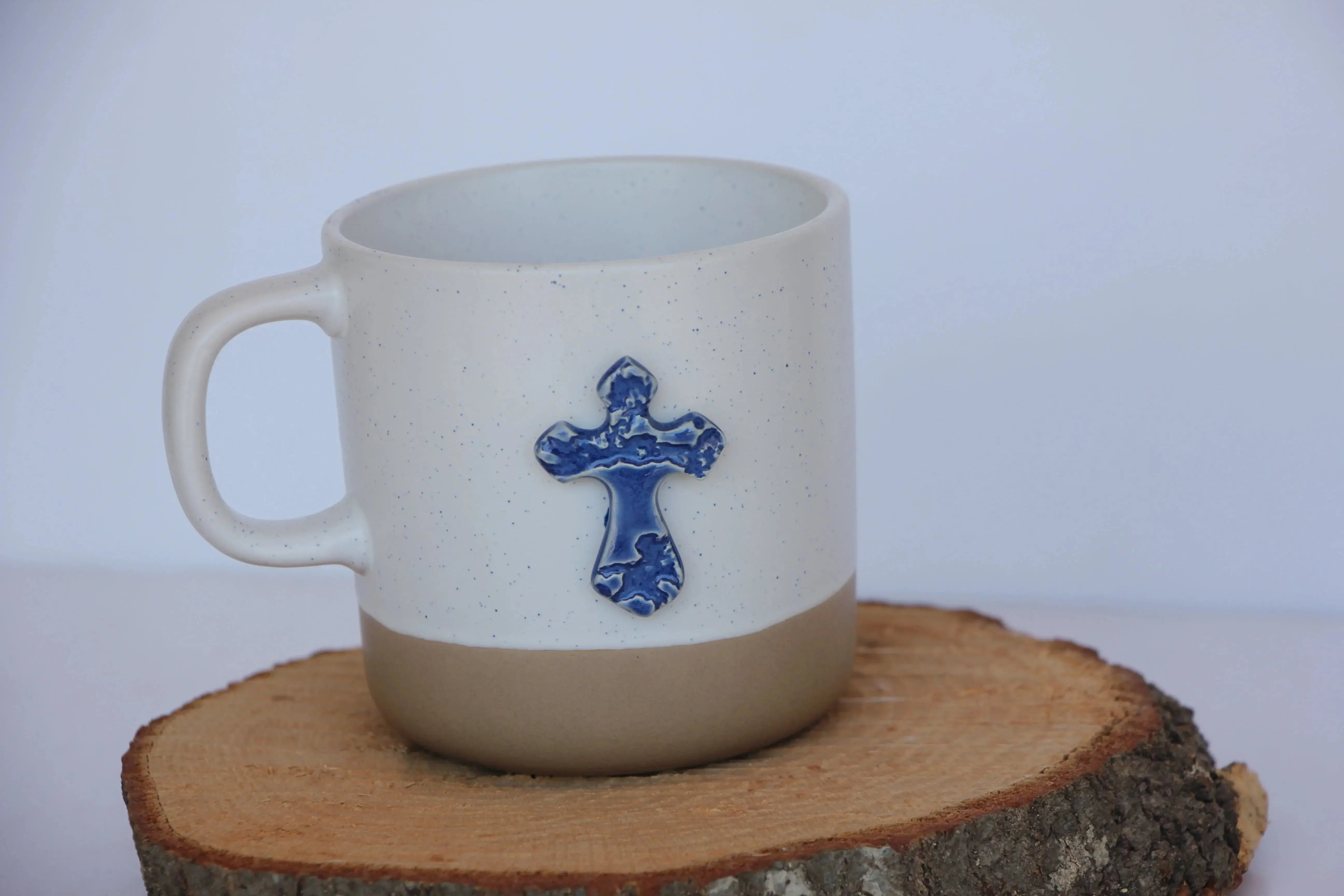 Speckled white ceramic mug with blue cross accent, farmhouse style home decor on wood slice