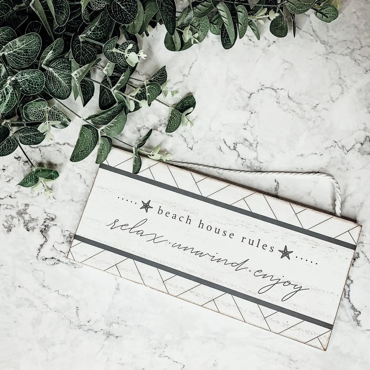 Beach house rules sign with relax unwind enjoy text, farmhouse decor on marble with greenery
