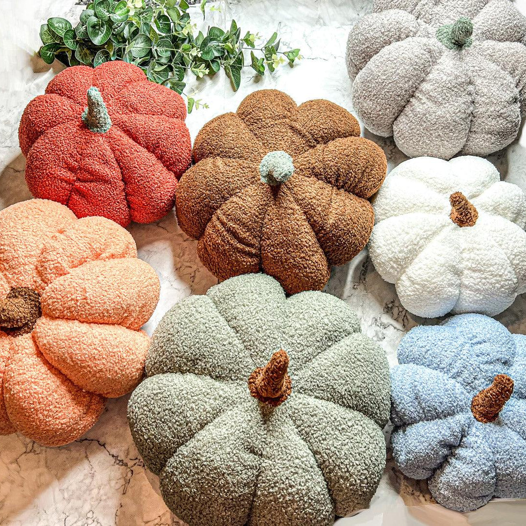 Colorful pumpkin-shaped cushions on a textured surface with greenery in the background.