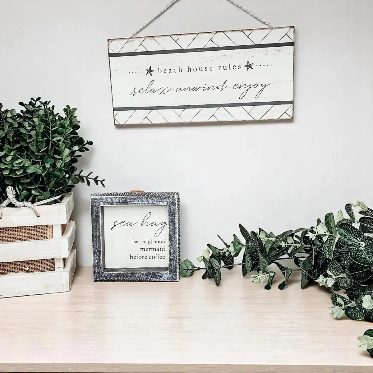 Beach house rules sign with relax unwind enjoy text, rustic decor, and greenery on wooden shelf