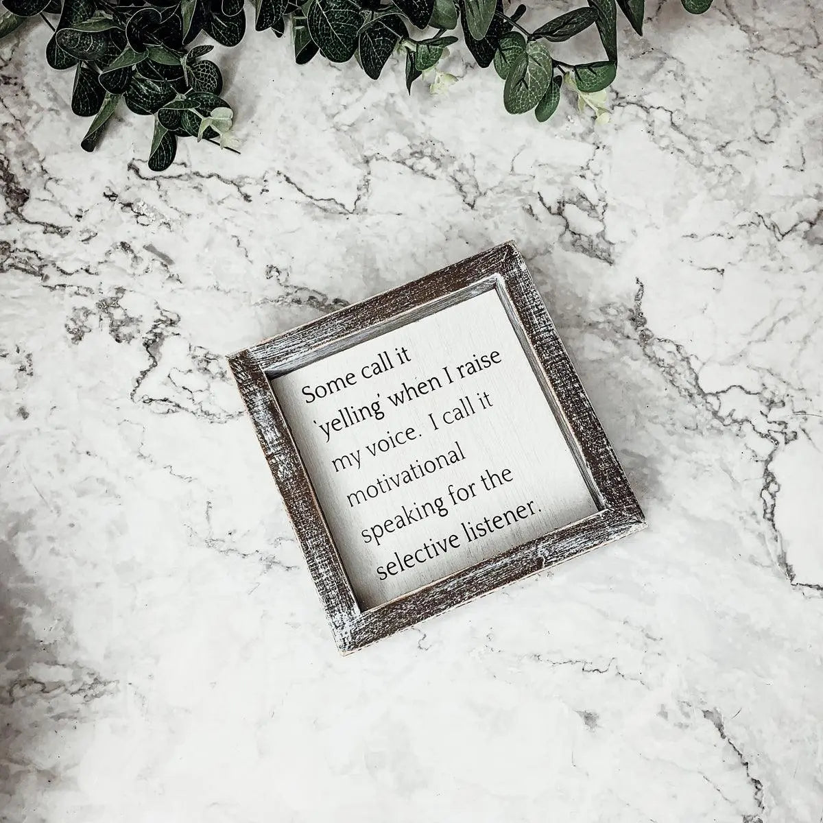 Decorative sign with motivational quote on a marble surface with greenery.