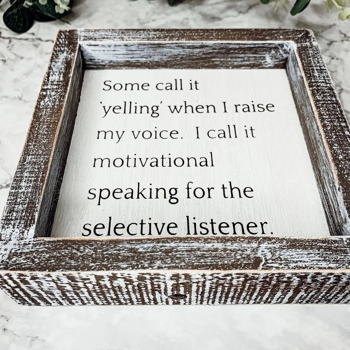 Wooden framed sign with humorous quote on a marble surface