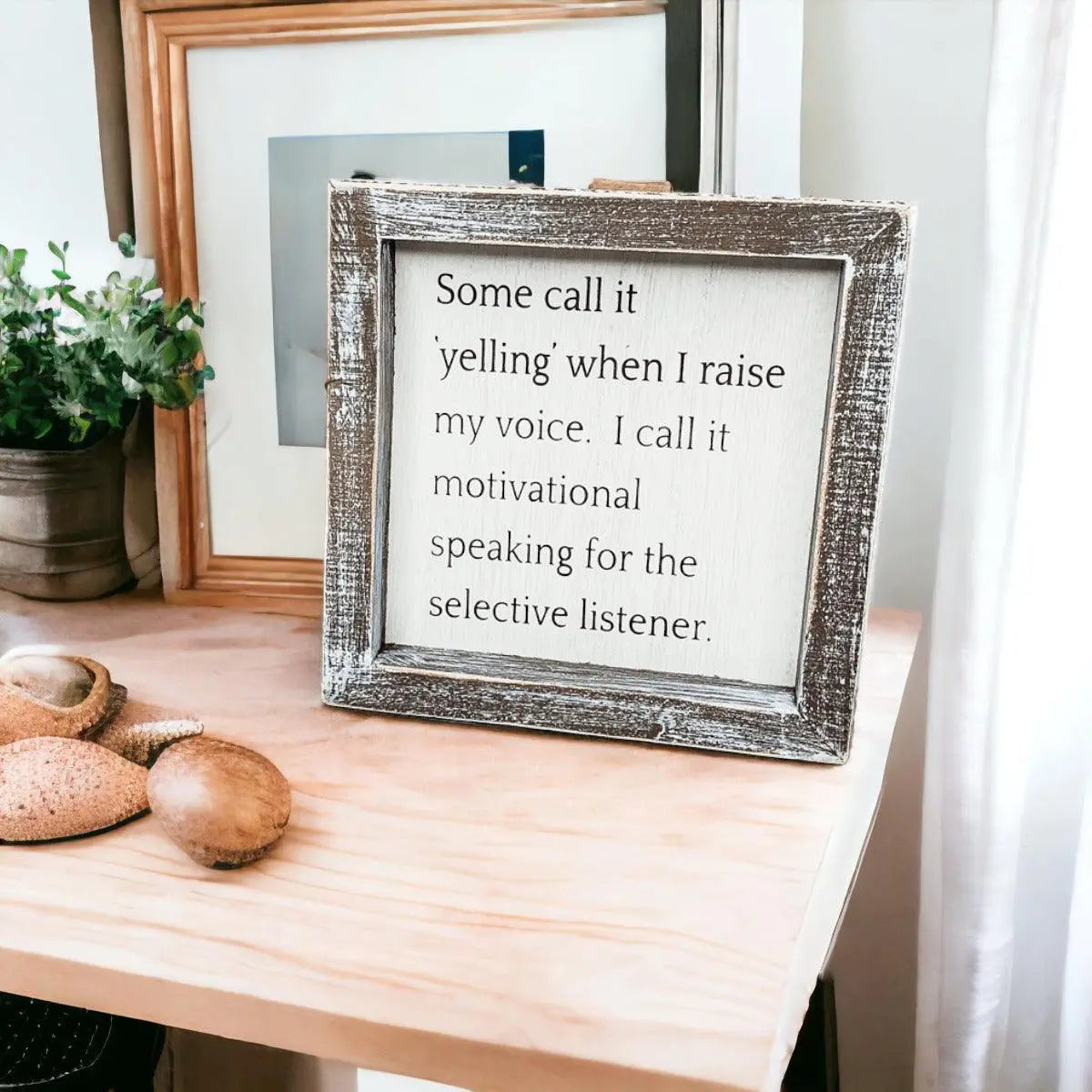 Framed motivational quote on a wooden surface with decorative items.