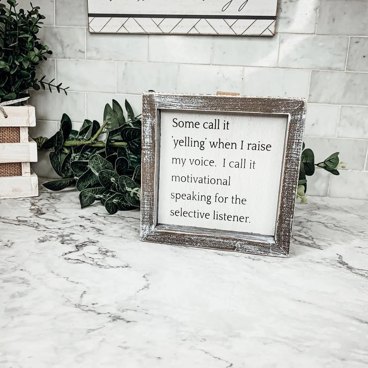 Framed motivational quote on a marble surface with plants in the background