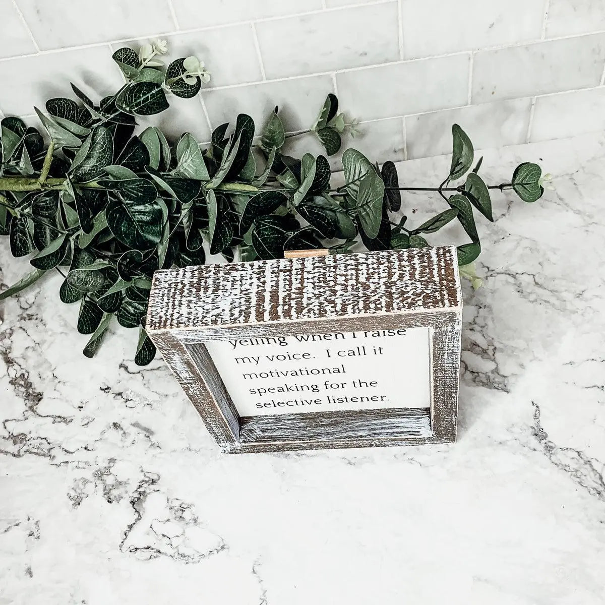 Decorative wooden box with a motivational quote on a marble surface with greenery.