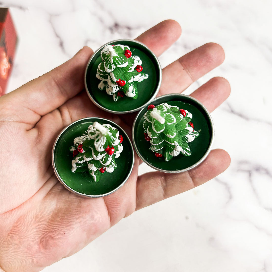 Three green containers with Christmas tree designs held in a hand against a white background