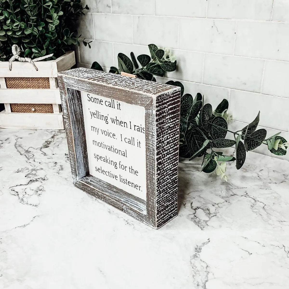 Wooden box with a motivational quote on a marble surface with plants in the background