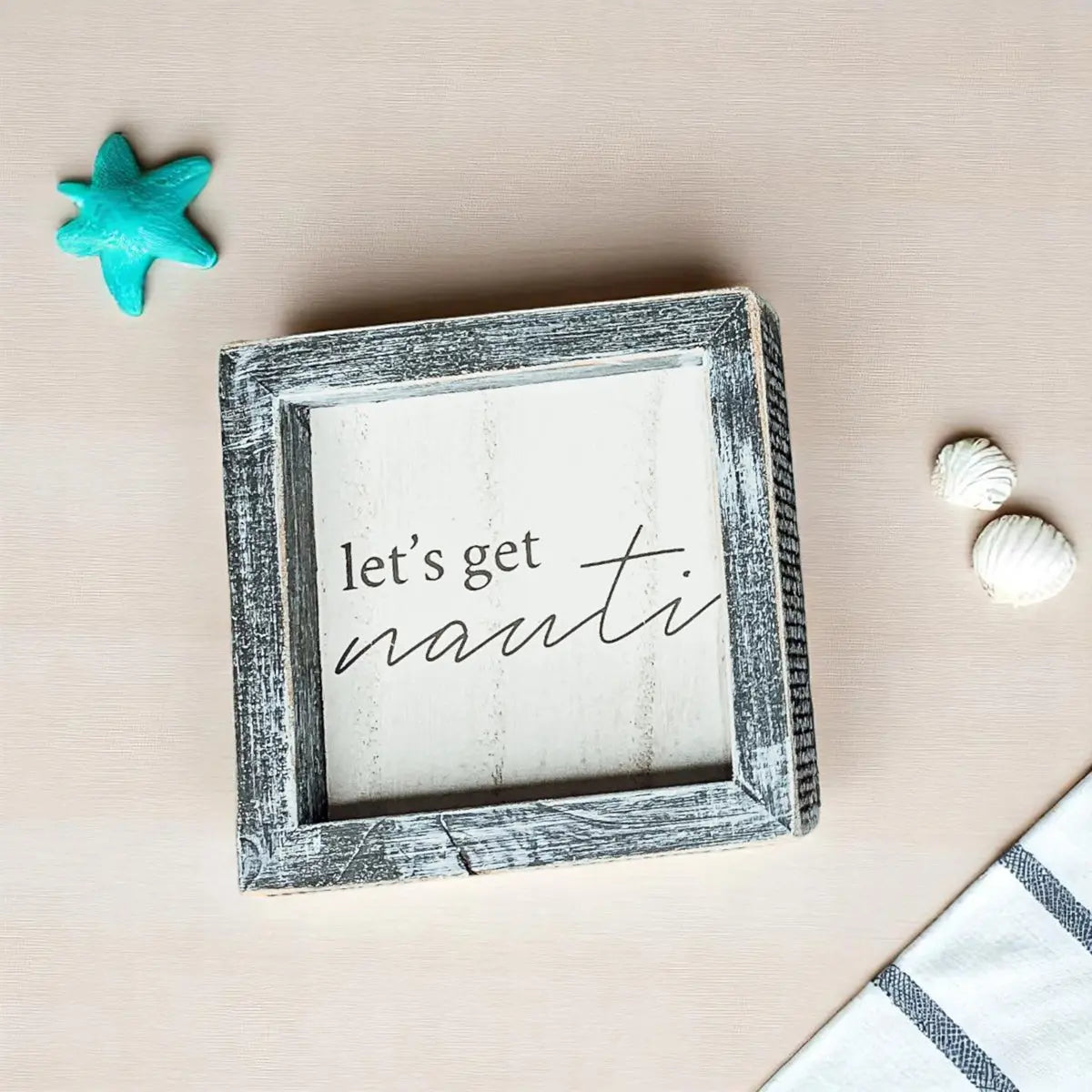 Decorative sign with 'let's get nauti' text on a beige background with starfish and shells.