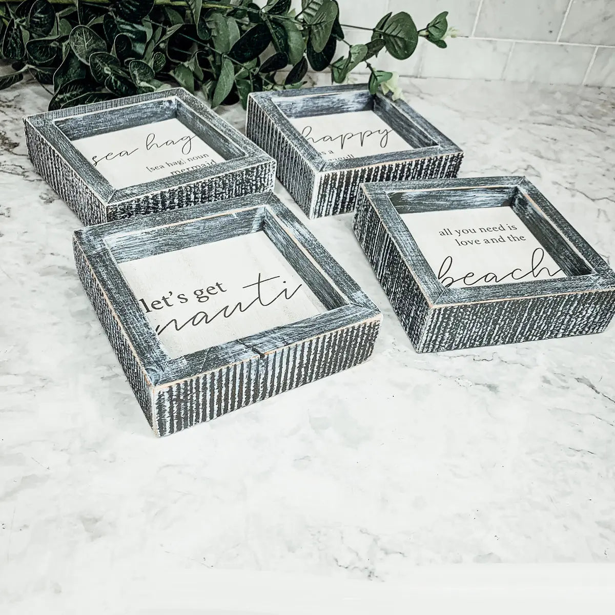 Set of four decorative boxes with rustic finishes and motivational phrases on a marble surface.