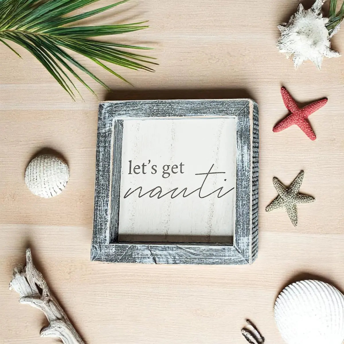 Decorative sign with 'let's get nauti' text on a wooden surface with beach-themed decor.