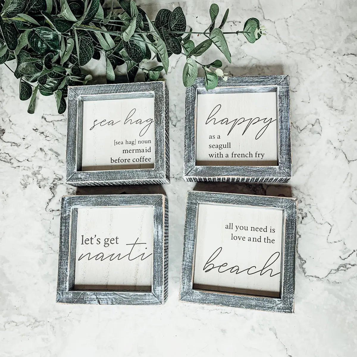 Four framed prints with beach-themed sayings on a marble surface.