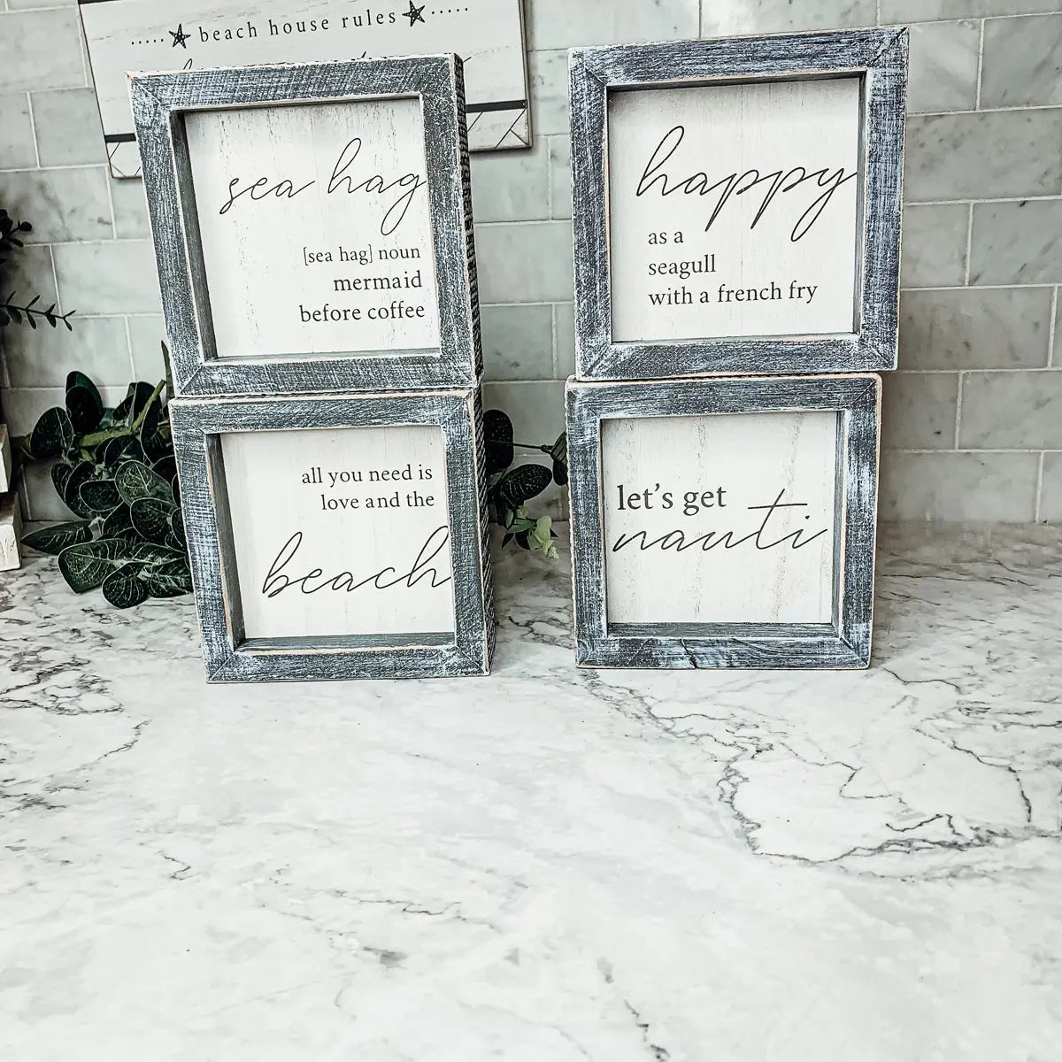 Four framed prints with beach-themed sayings on a marble surface.