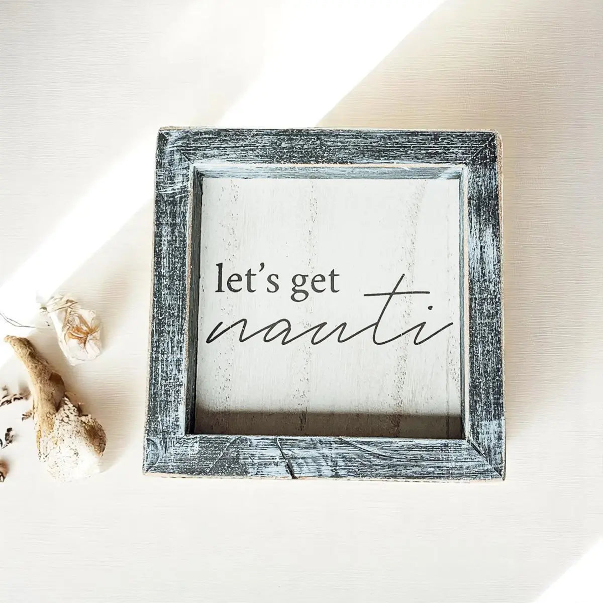 Decorative sign with 'let's get nauti' text in a rustic frame on a neutral background