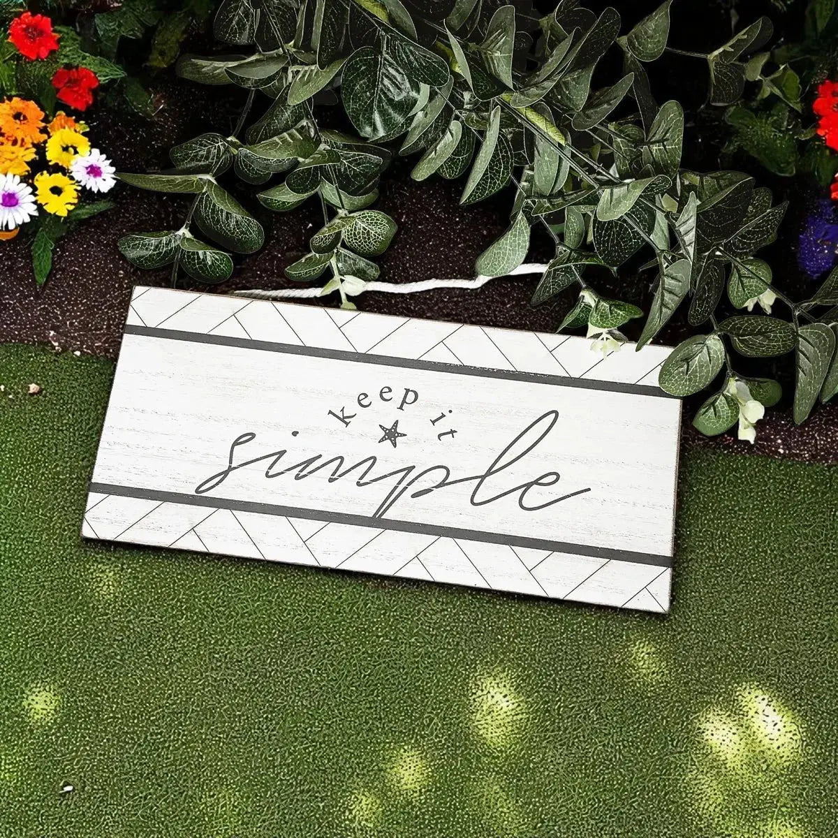 Decorative sign with 'keep it simple' text on a grassy background with flowers.