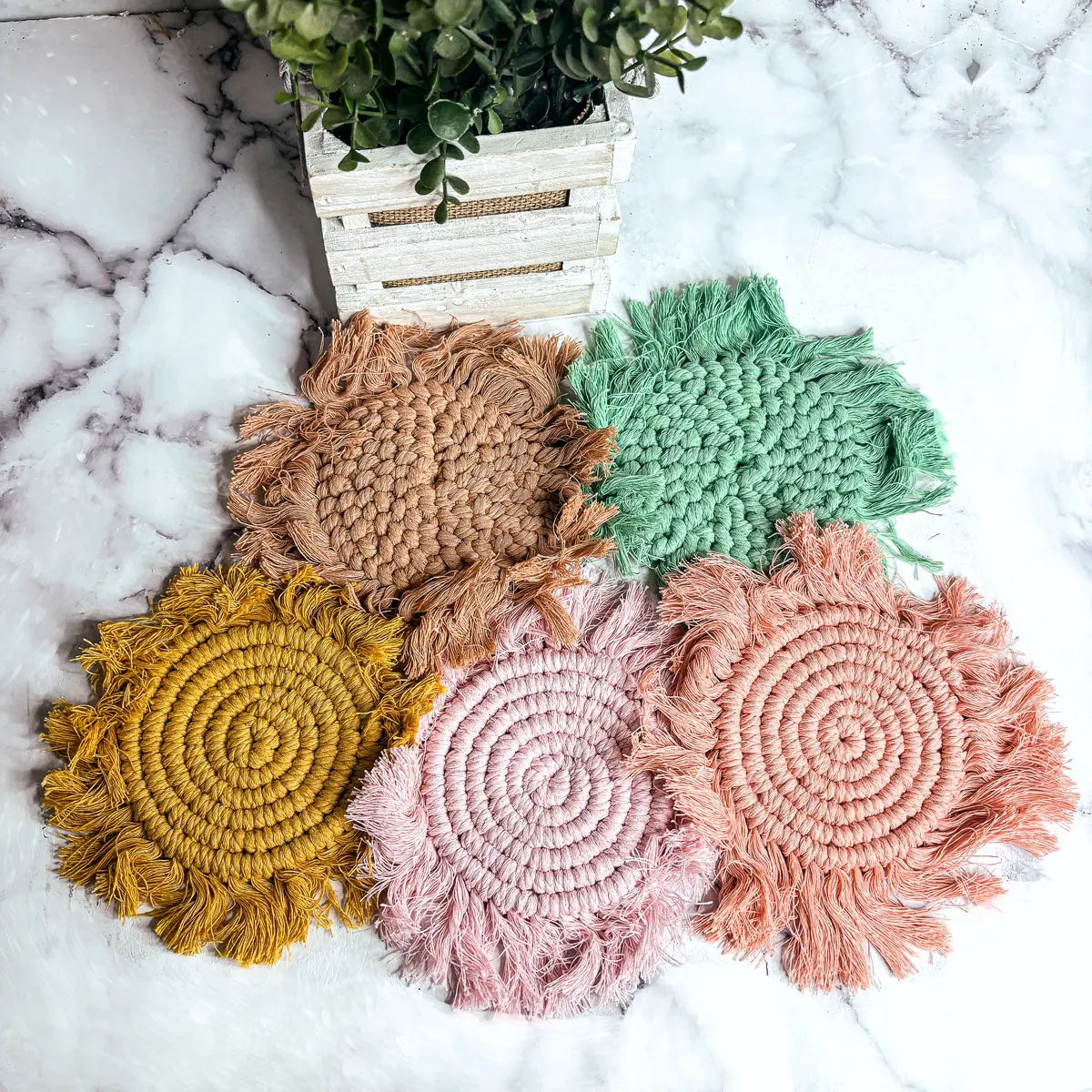 Set of colorful crocheted coasters on a marble surface with a plant in the background.