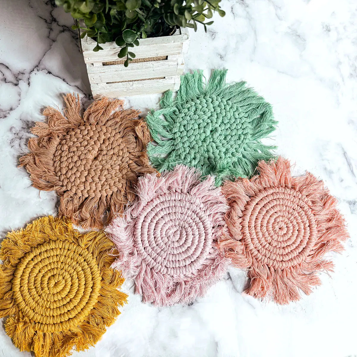 Set of colorful woven coasters on a marble surface with a plant in the background.