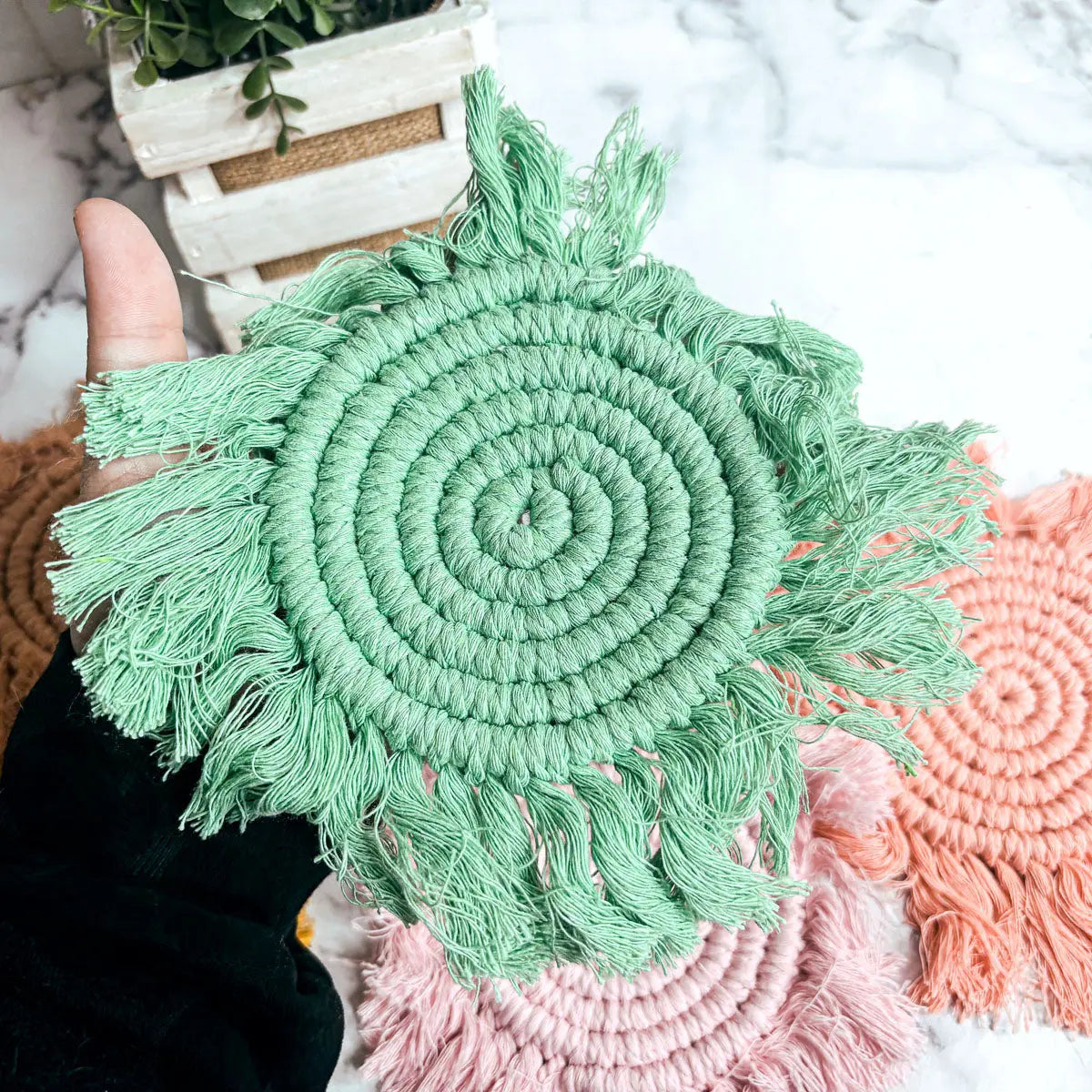 Handmade green macrame coaster held by a hand with a blurred background