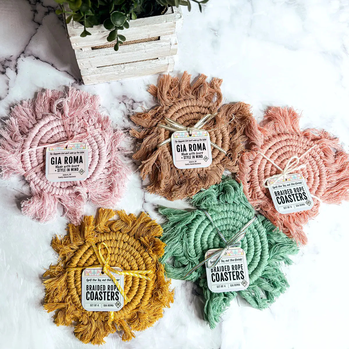 Five braided rope coasters in pink, brown, green, and yellow on a white surface with 'Gia Roma' branding.
