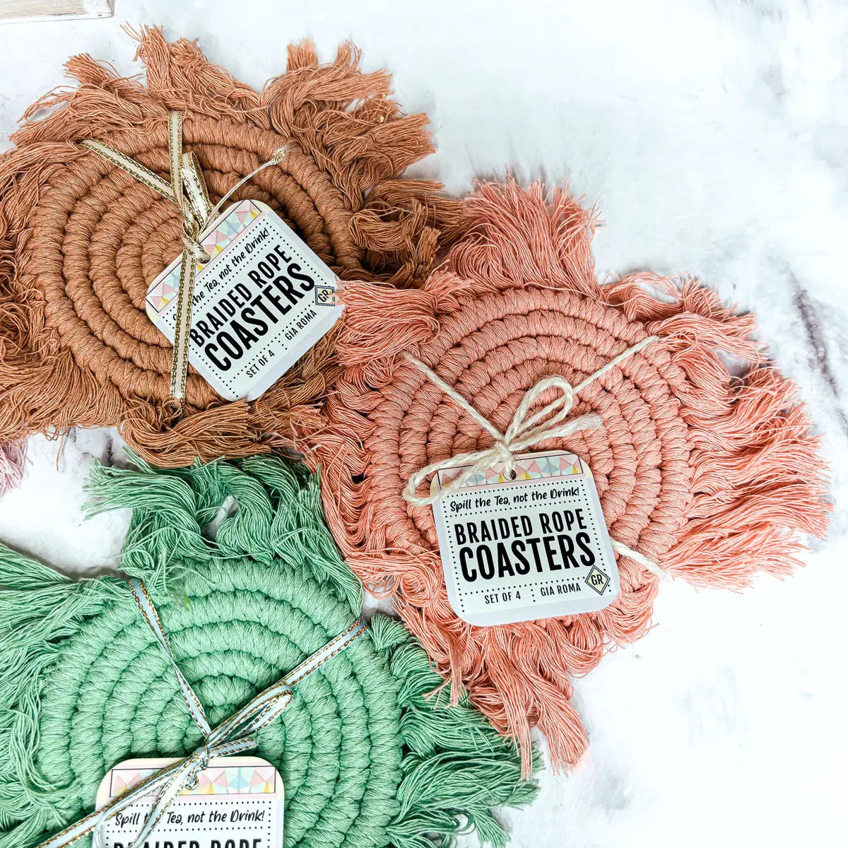 Set of braided rope coasters in brown, pink, and green with tags on a white background.