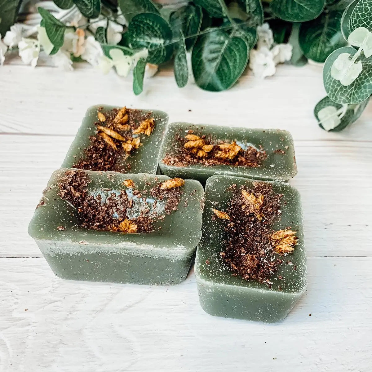 Green soap bars with decorative elements on a white wooden surface with greenery in the background