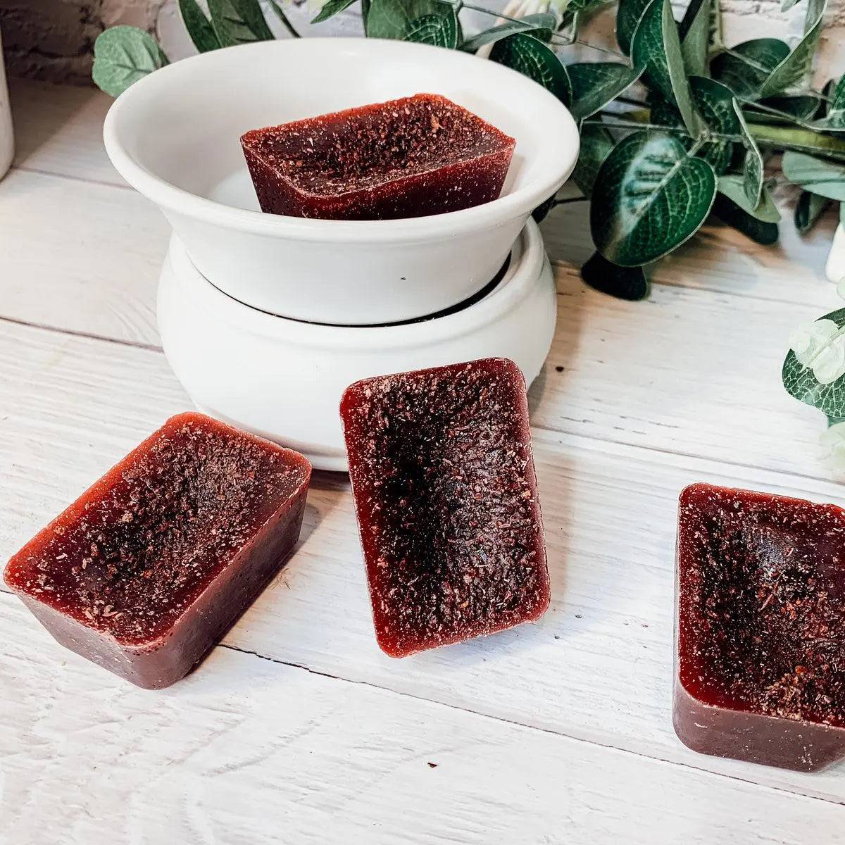 Red soap bars on a white surface with a white bowl and plant in the background