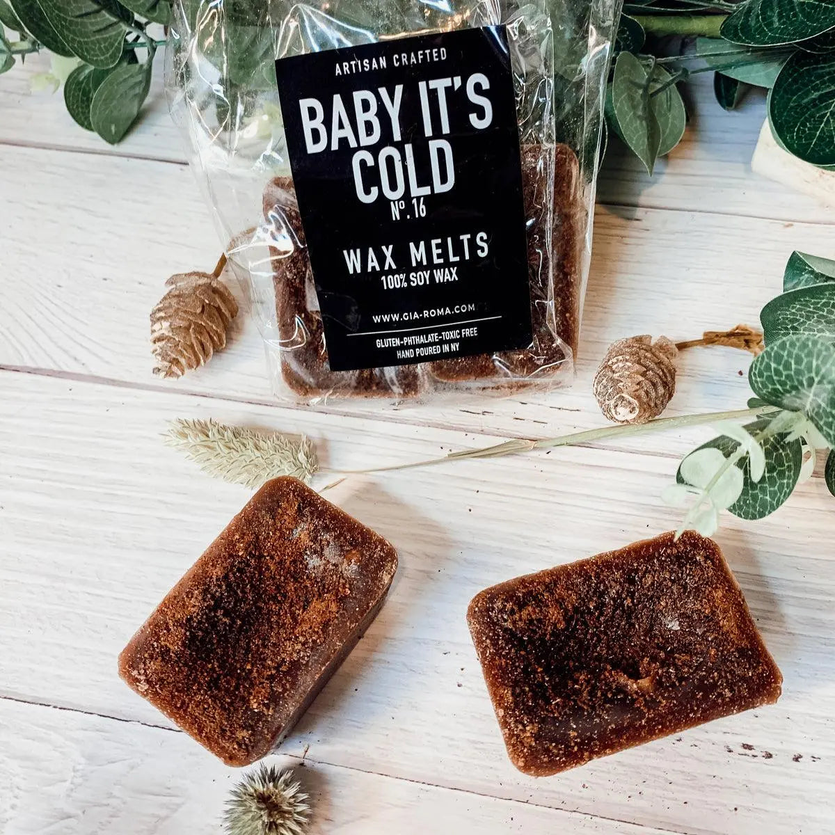 Two wax melts on a wooden surface with a 'Baby It's Cold' wax melts packaging in the background.