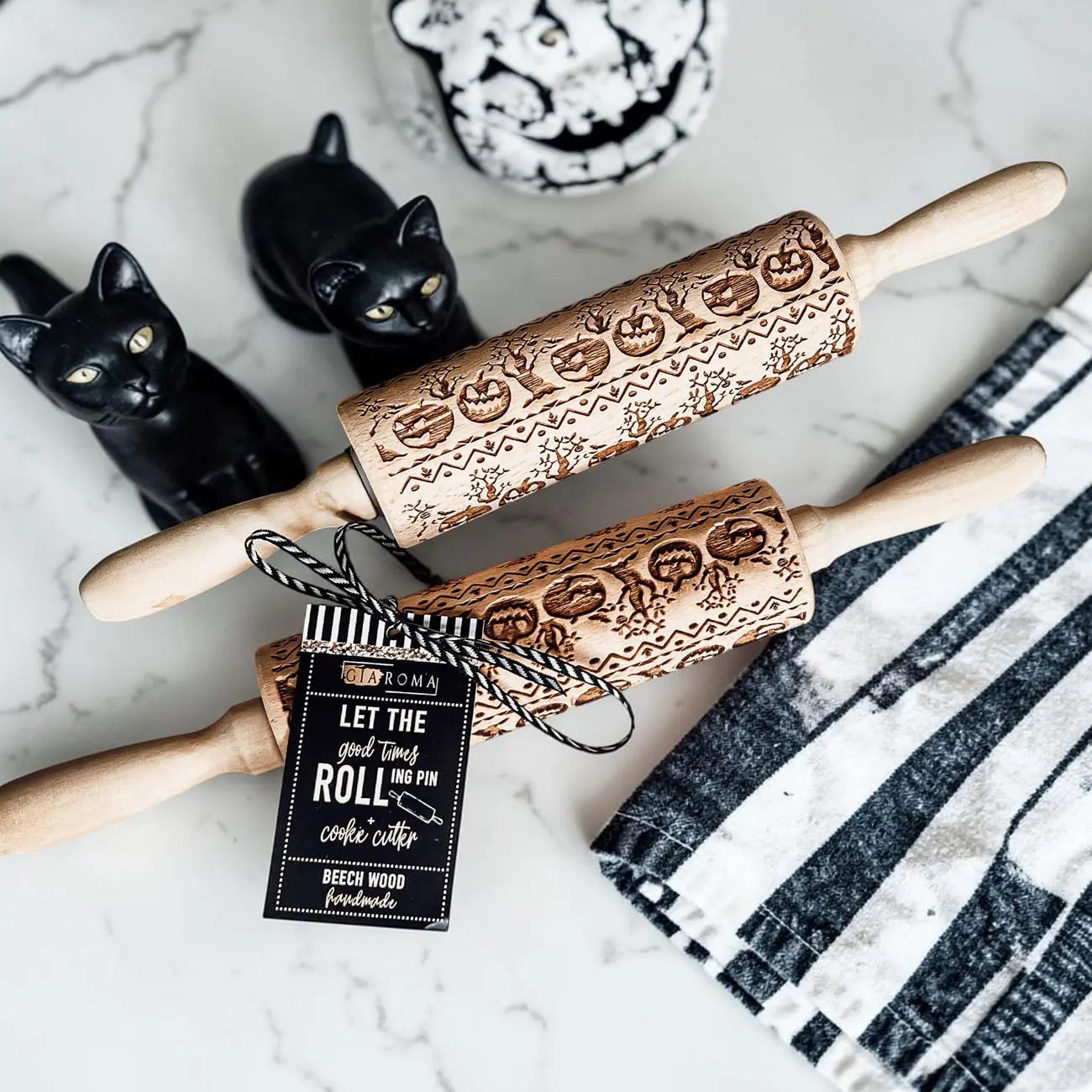 Two wooden rolling pins with Halloween designs on a marble surface with black cats and a cake.
