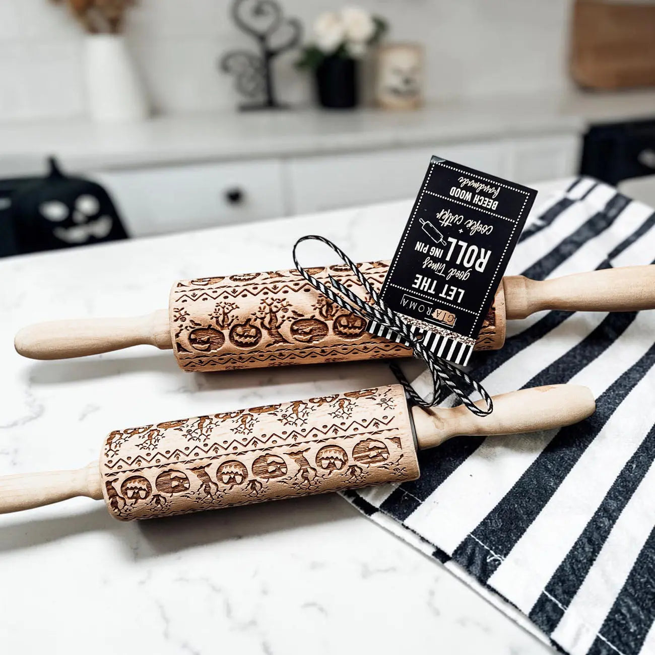 Two wooden rolling pins with embossed designs on a marble surface with a striped cloth.