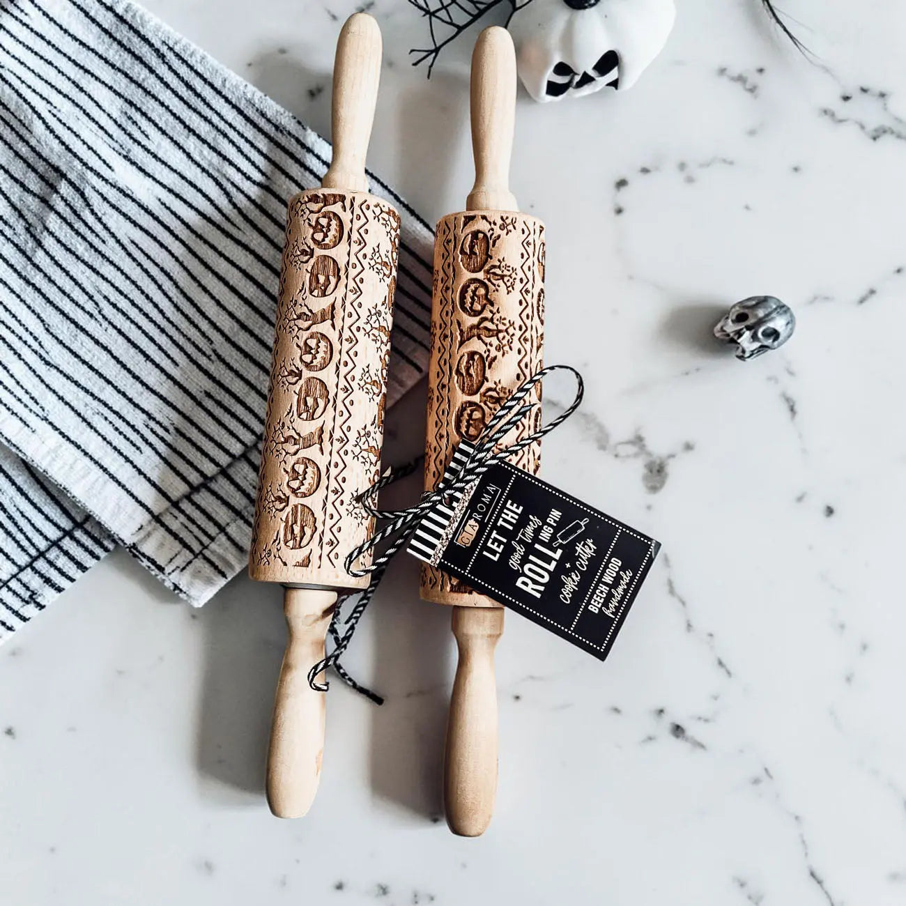 Two wooden embossed rolling pins with decorative patterns on a marble surface.