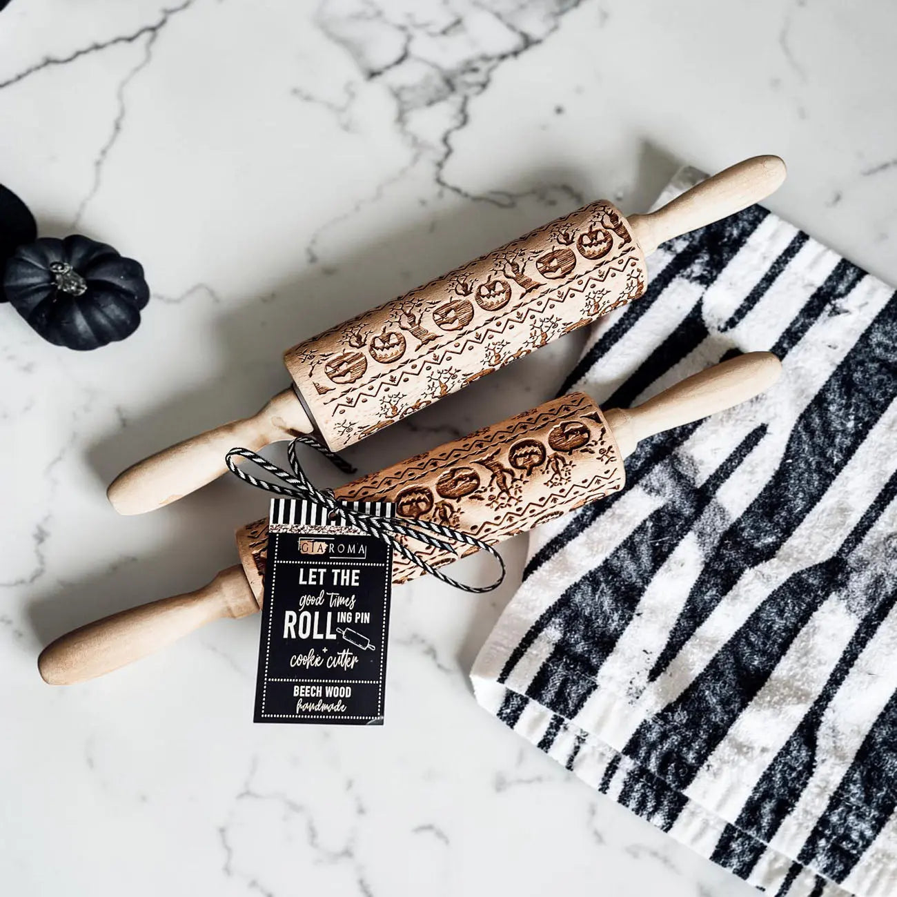 Wooden rolling pins with embossed designs on a marble surface with a black and white striped towel.