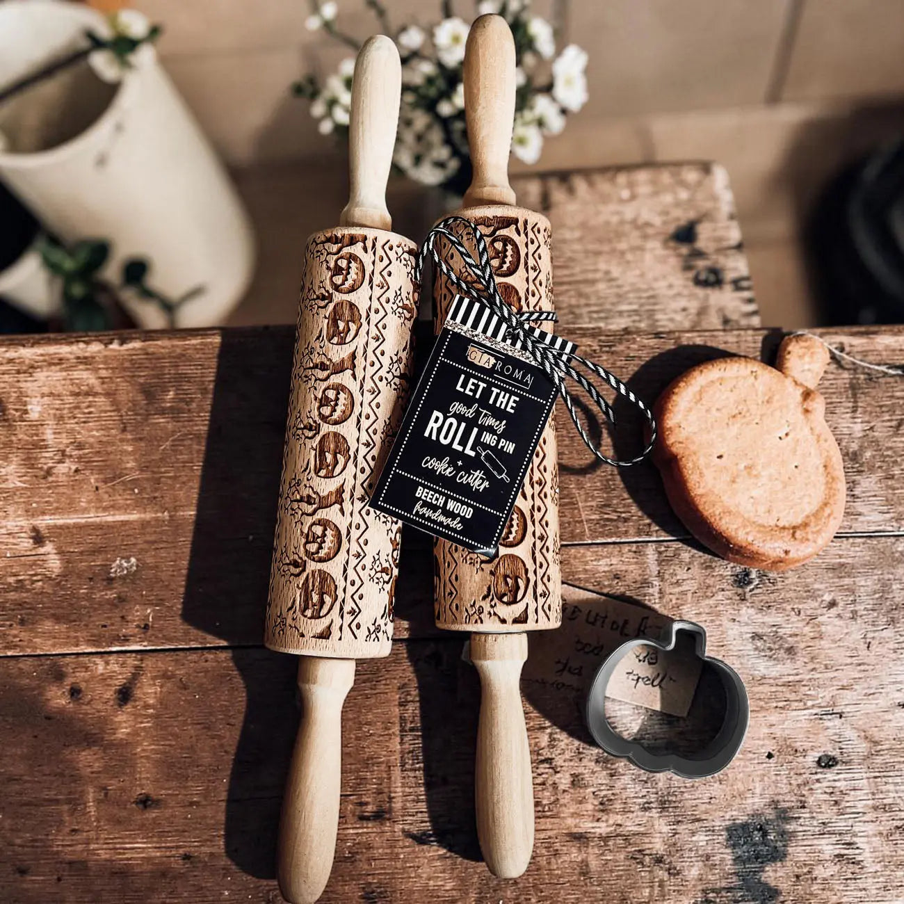 Two wooden embossing rolling pins with engraved patterns on a rustic wooden surface, accompanied by a cookie cutter and a decorative tag.