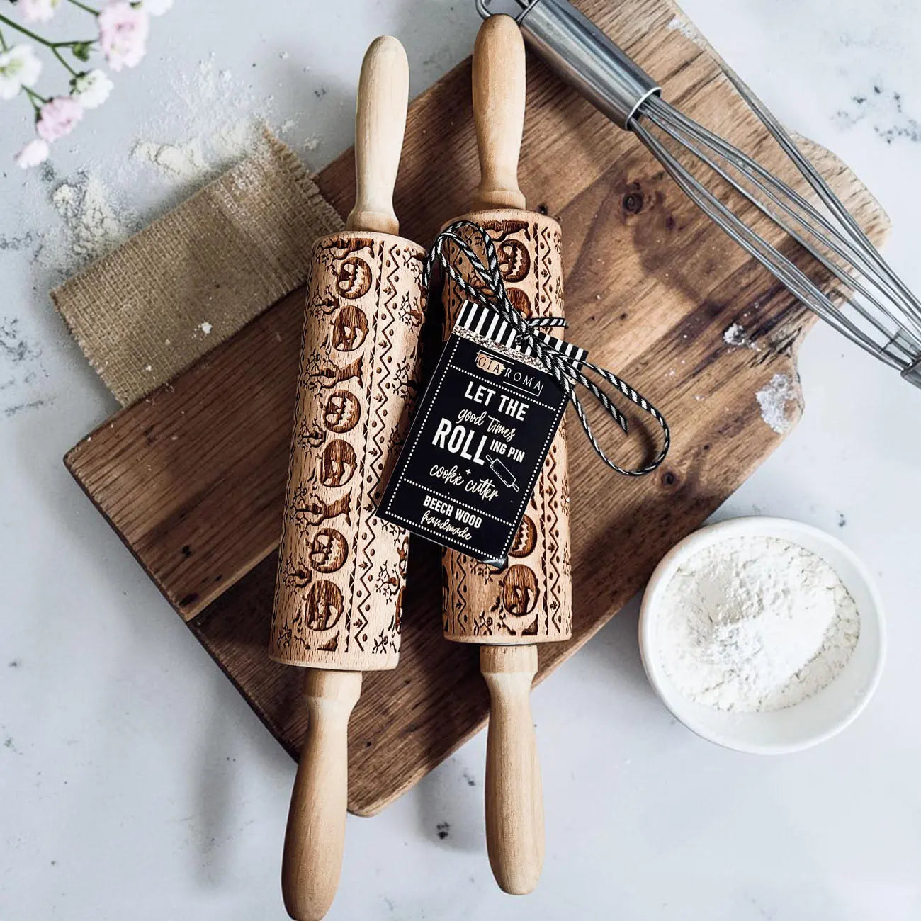 Two wooden embossed rolling pins on a wooden board with a tag and flour bowl.
