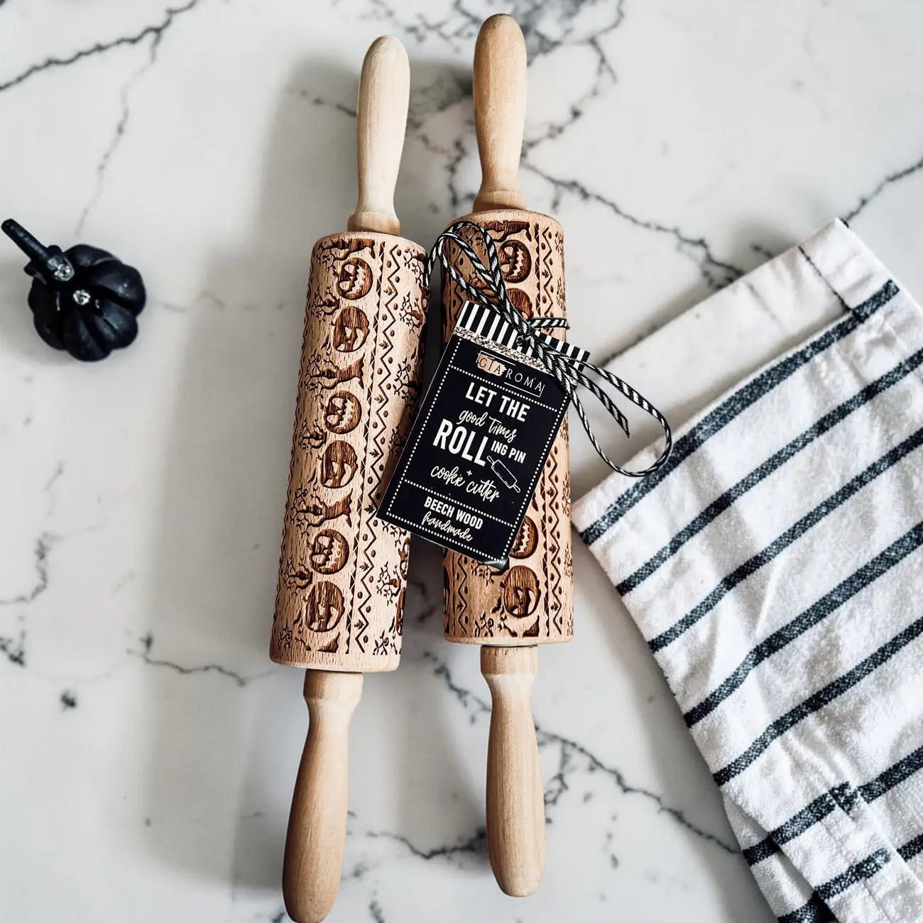 Two wooden embossed rolling pins with decorative patterns on a marble surface with a kitchen towel.