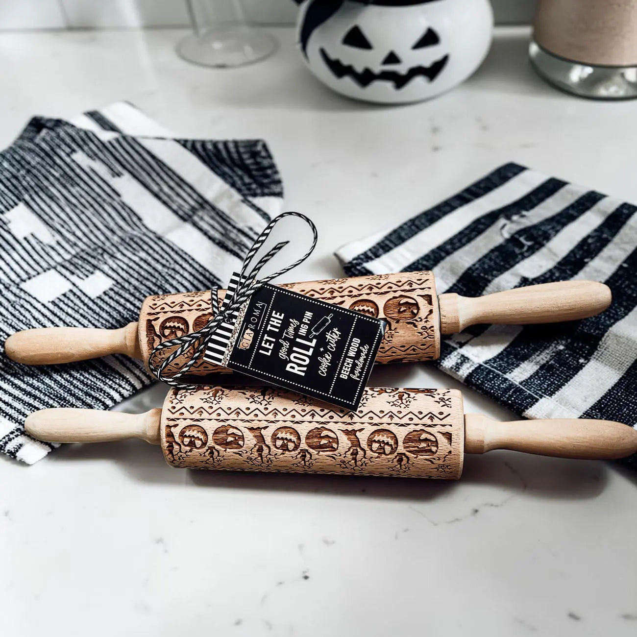 Two wooden rolling pins with Halloween designs on a marble surface with striped cloths.