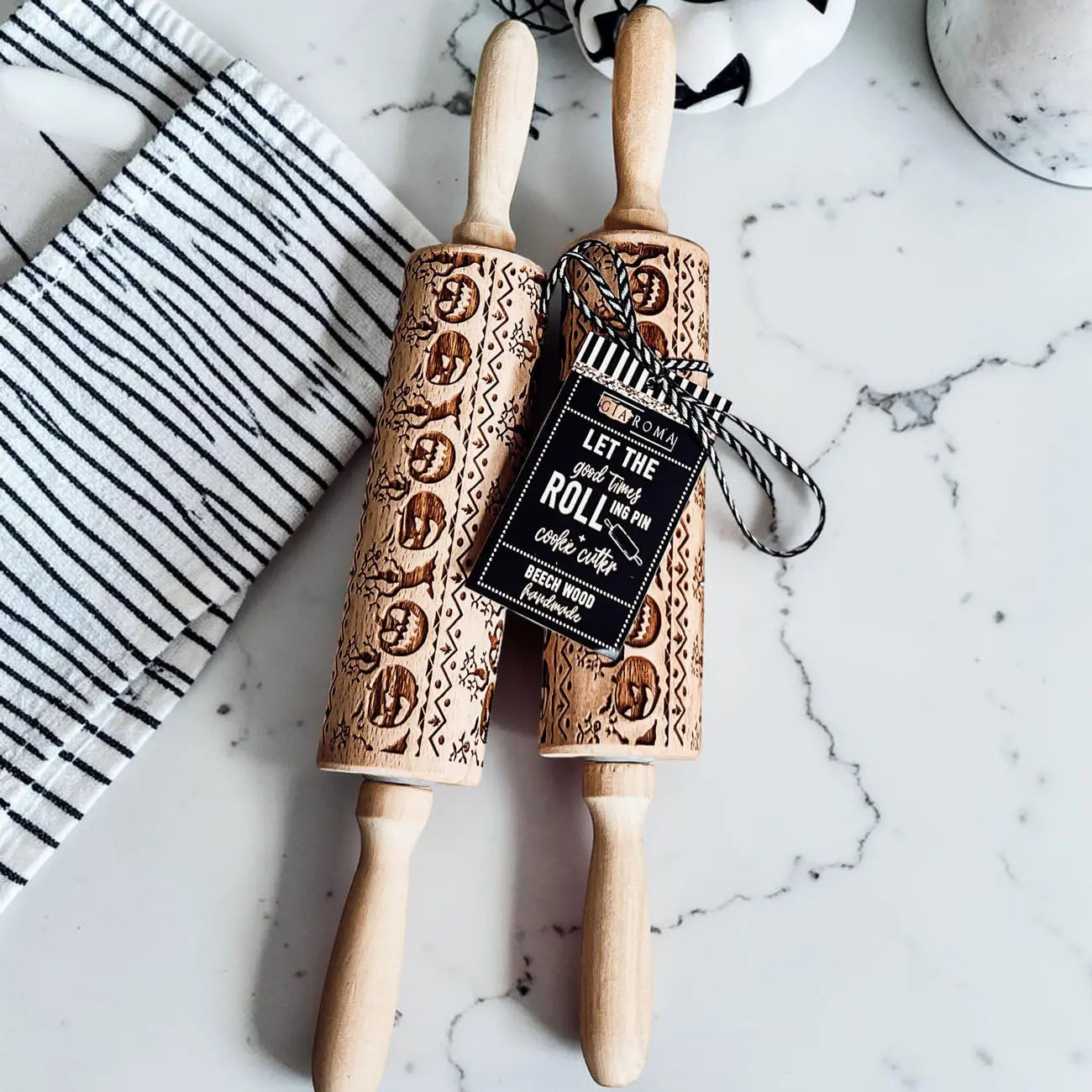 Two wooden embossed rolling pins with decorative patterns on a marble surface.