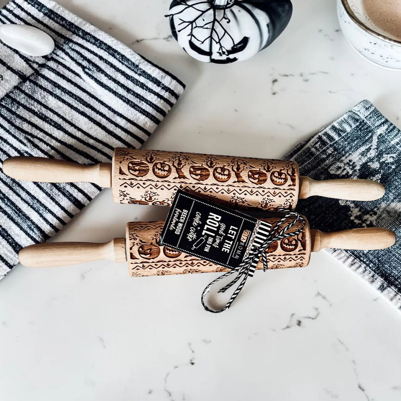 Two wooden rolling pins with embossed designs on a marble surface with a towel and cup in the background.