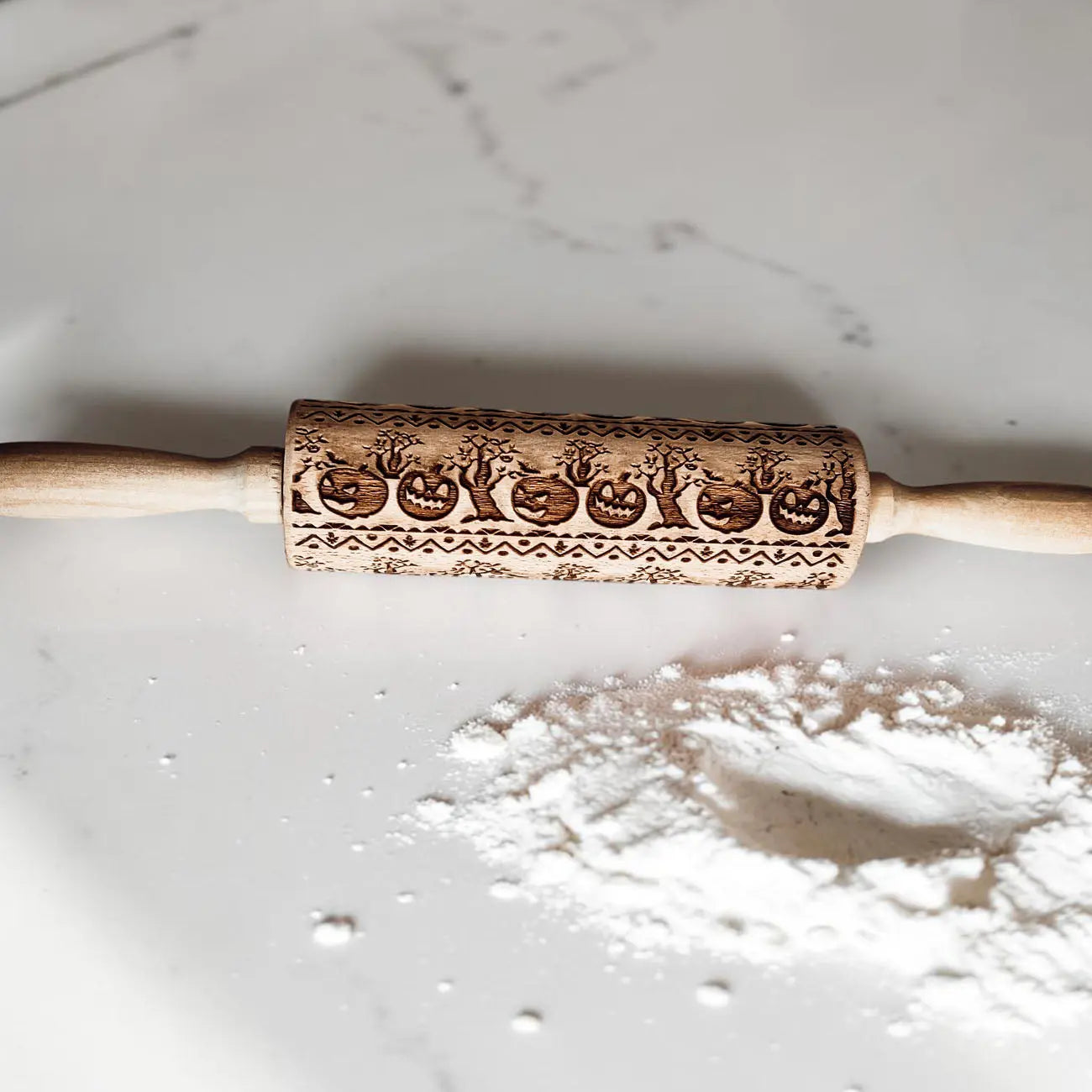 Wooden rolling pin with embossed designs on a marble surface