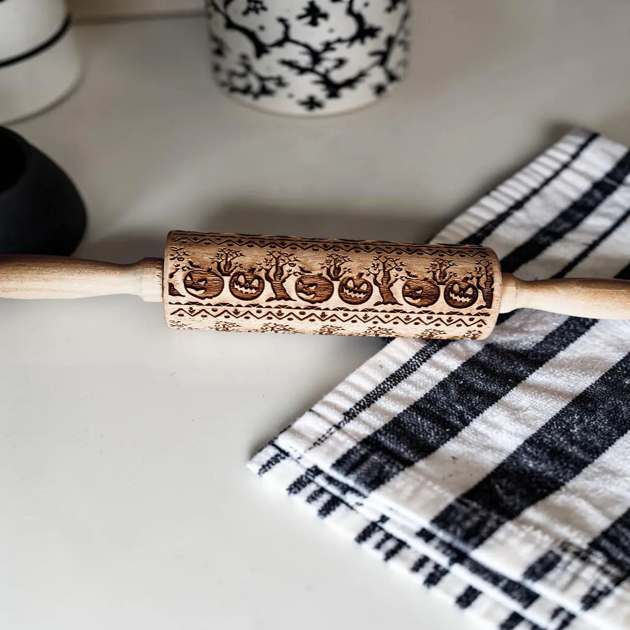 Wooden rolling pin with embossed designs on a checkered towel