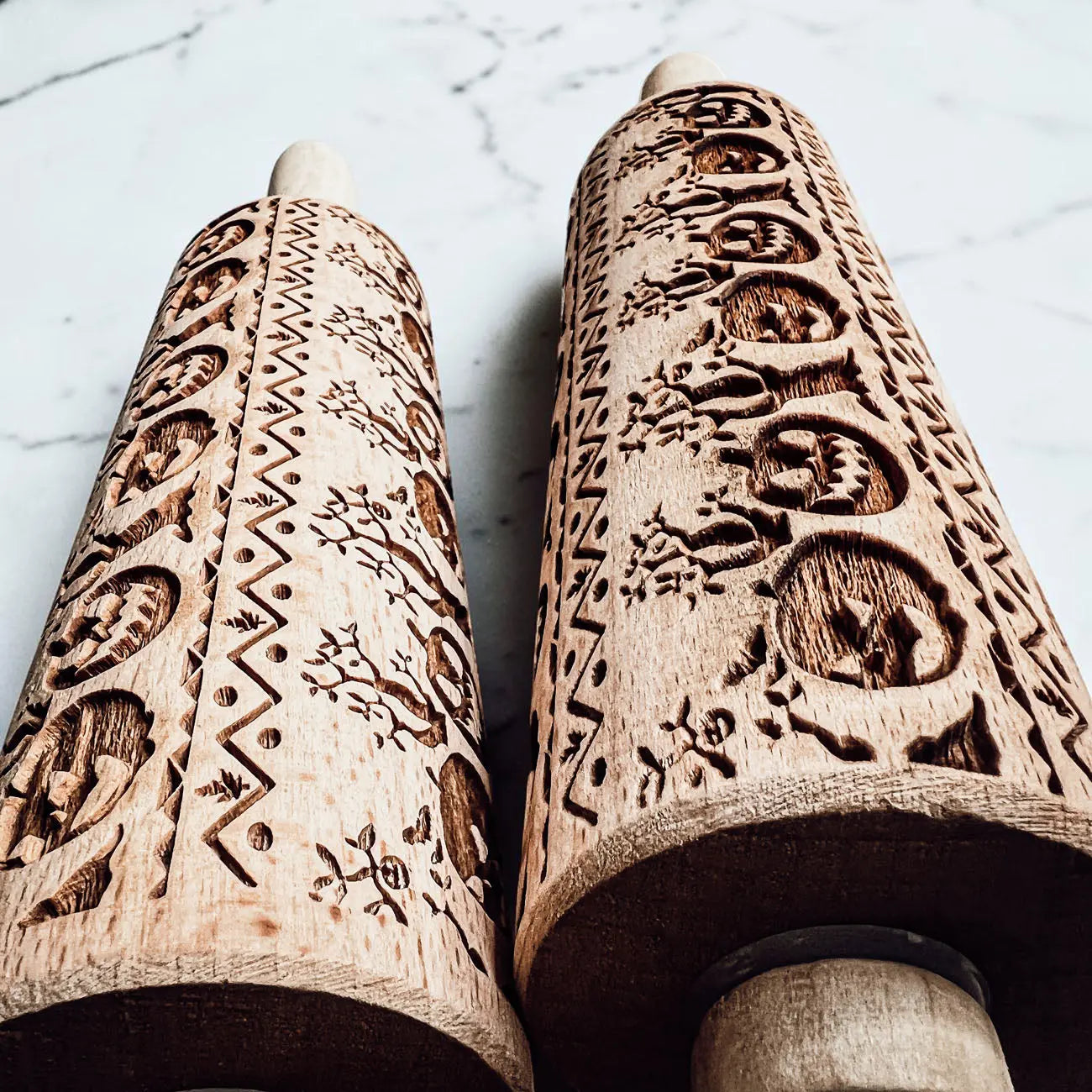 Two wooden rolling pins with intricate carvings on a light background