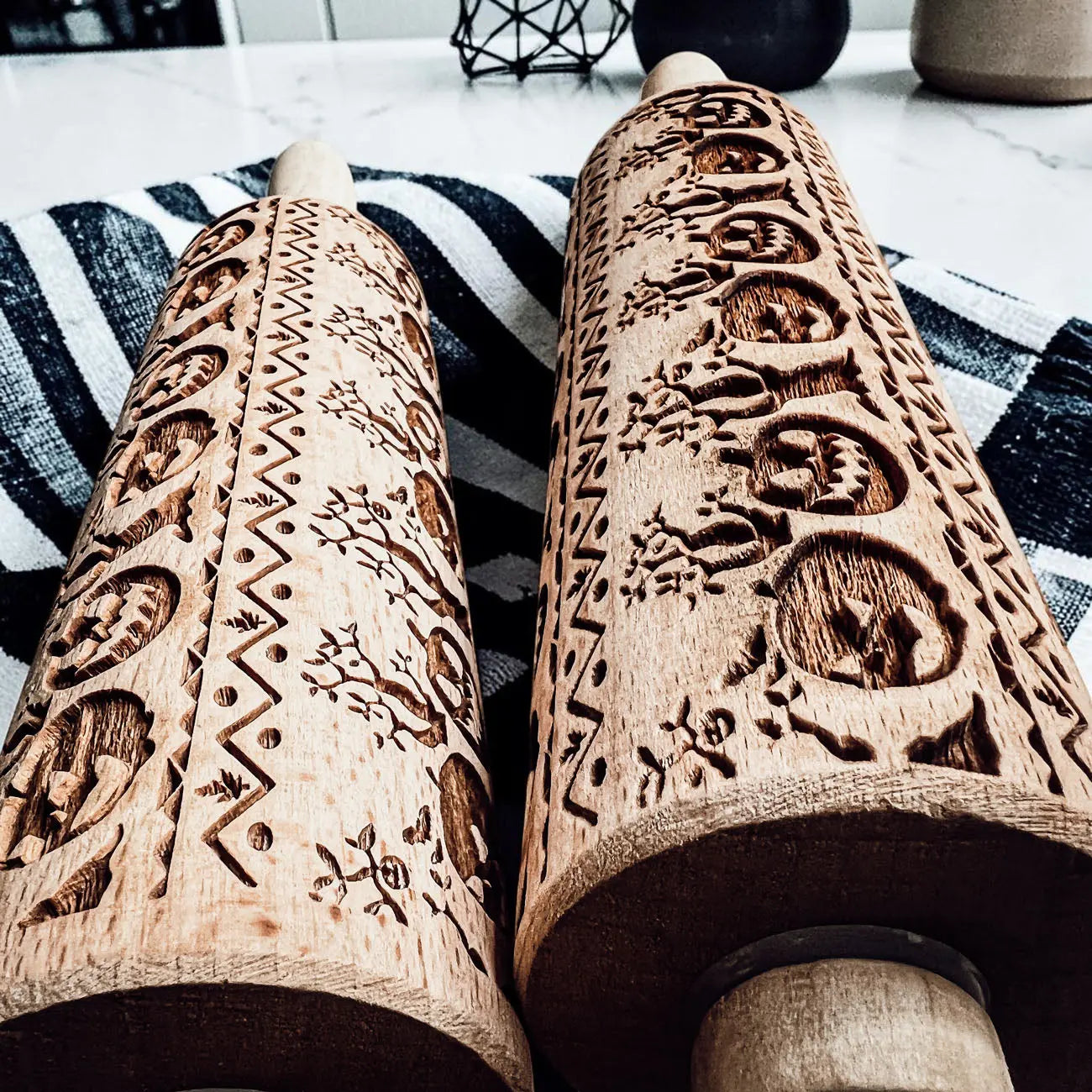 Two wooden embossing rolling pins with intricate patterns on a striped fabric background.